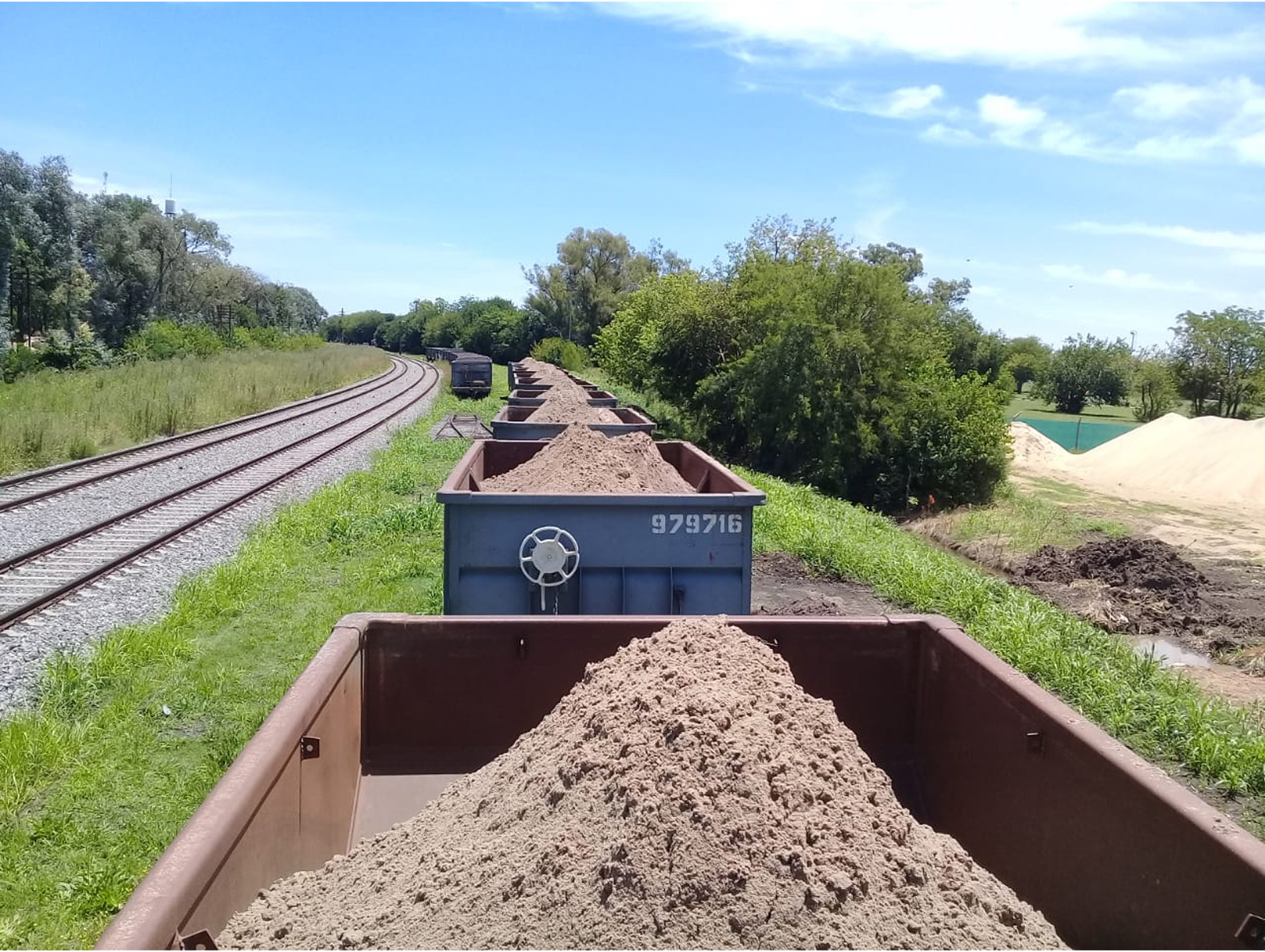 Vagones de tren de carga transportando arena en vías férreas.