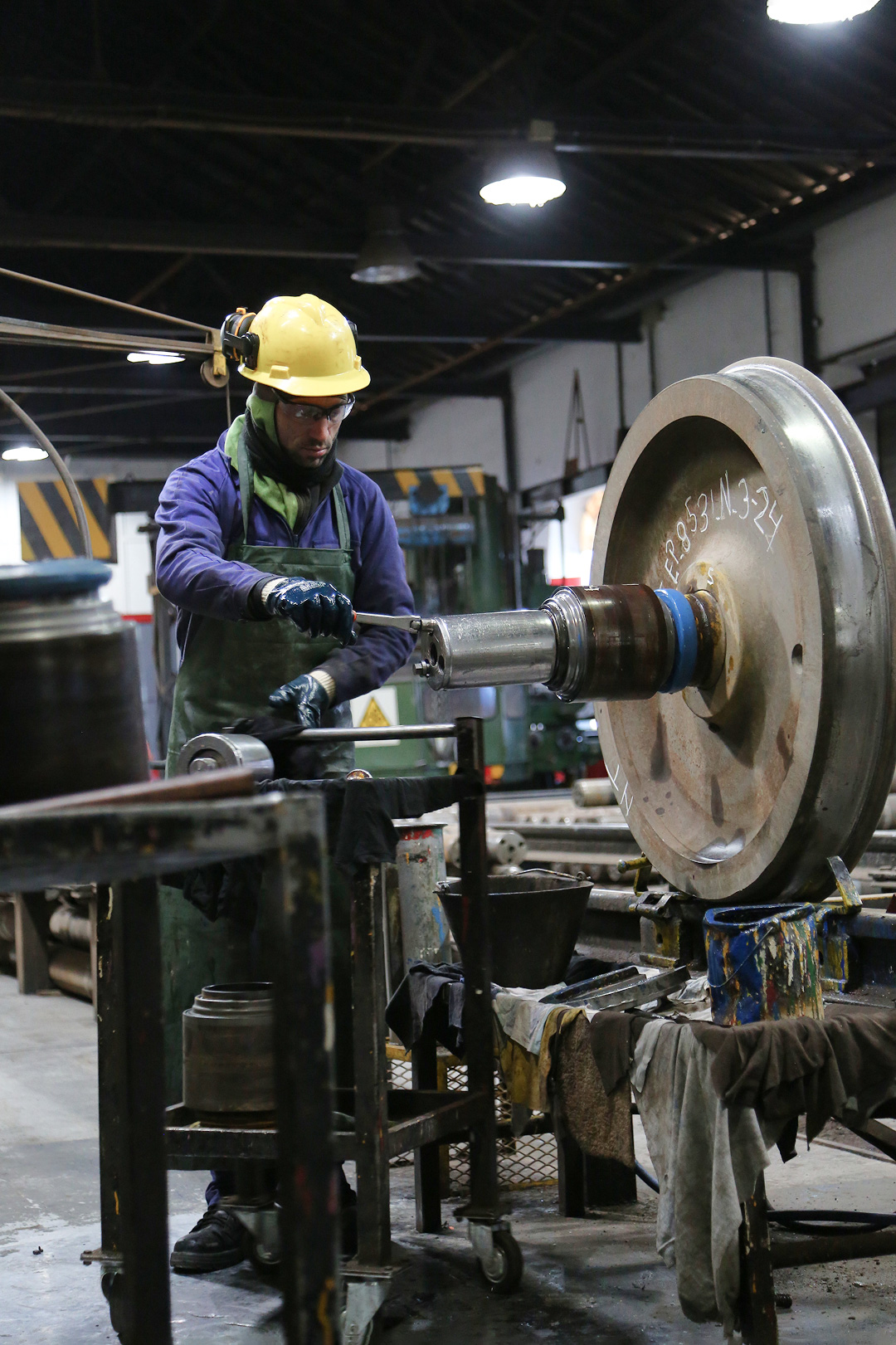 Imagen de trabajador ferroviario con casco y guantes realizando mantenimiento de una rueda de tren en taller.