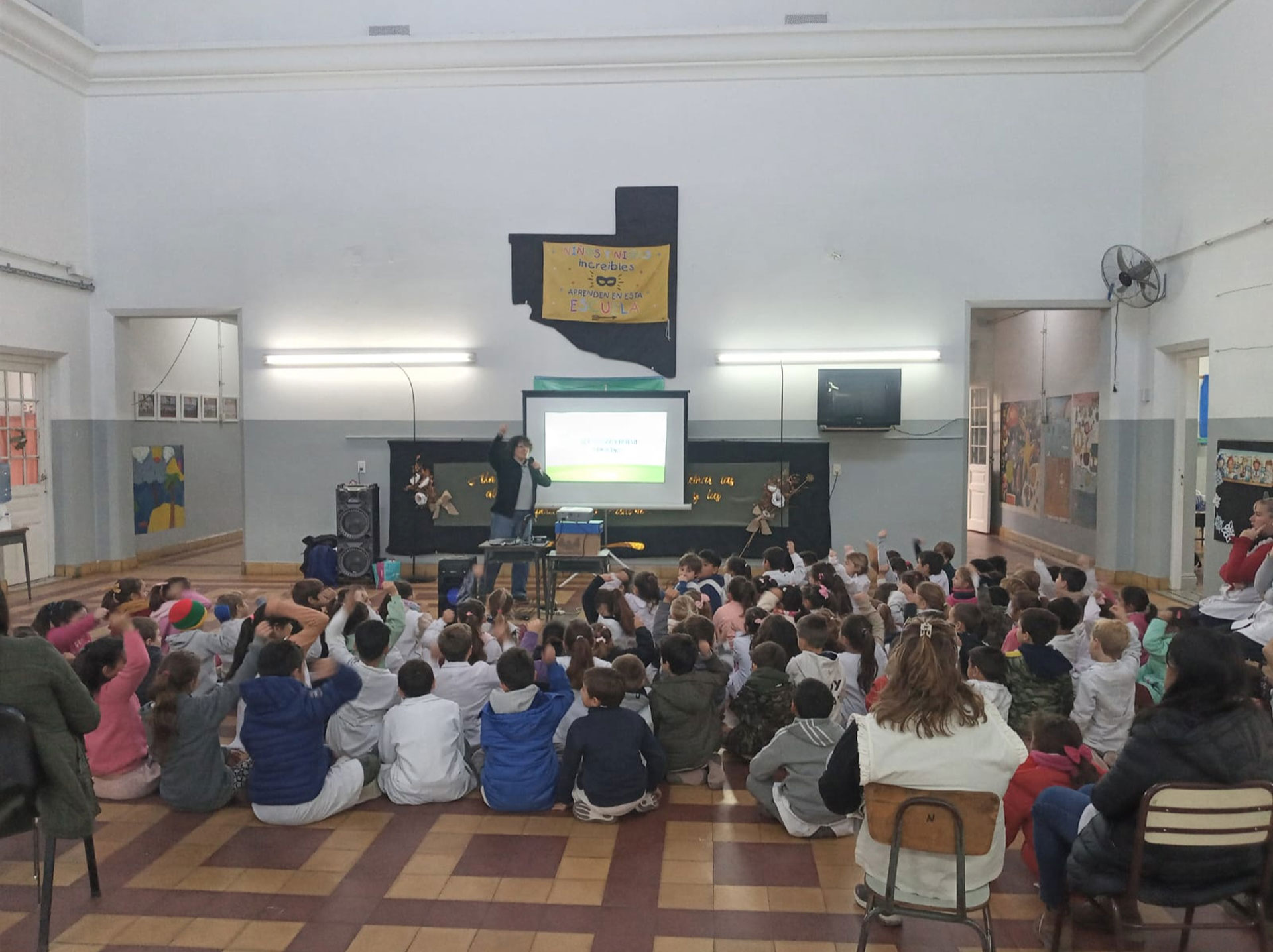 Capacitación en un jardín, con niños sentados en el piso frente a una pantalla y docentes guiando la actividad.