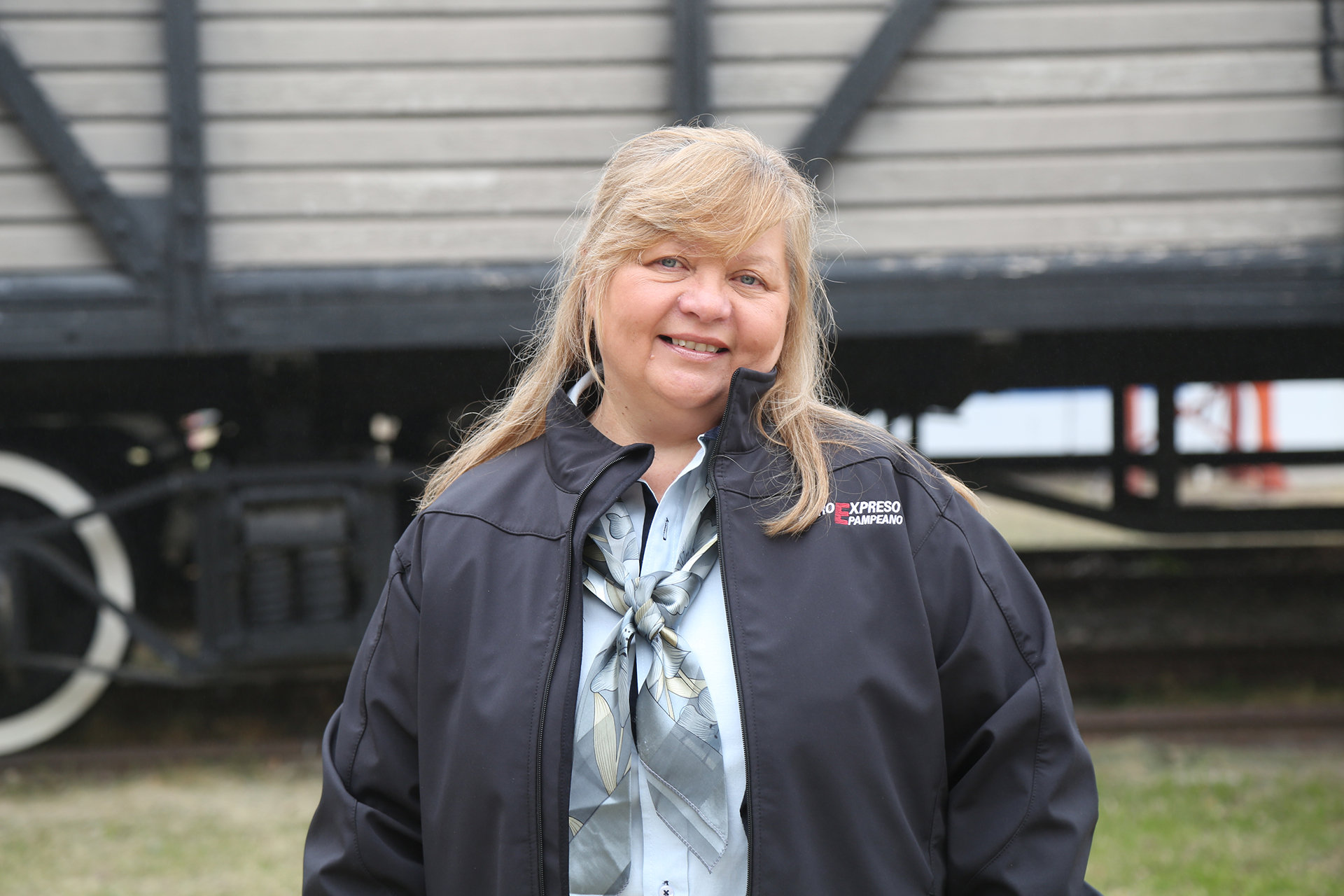 Colaboradora de Ferroexpreso Pampeano posando con uniforme corporativo frente a un vagón de tren.